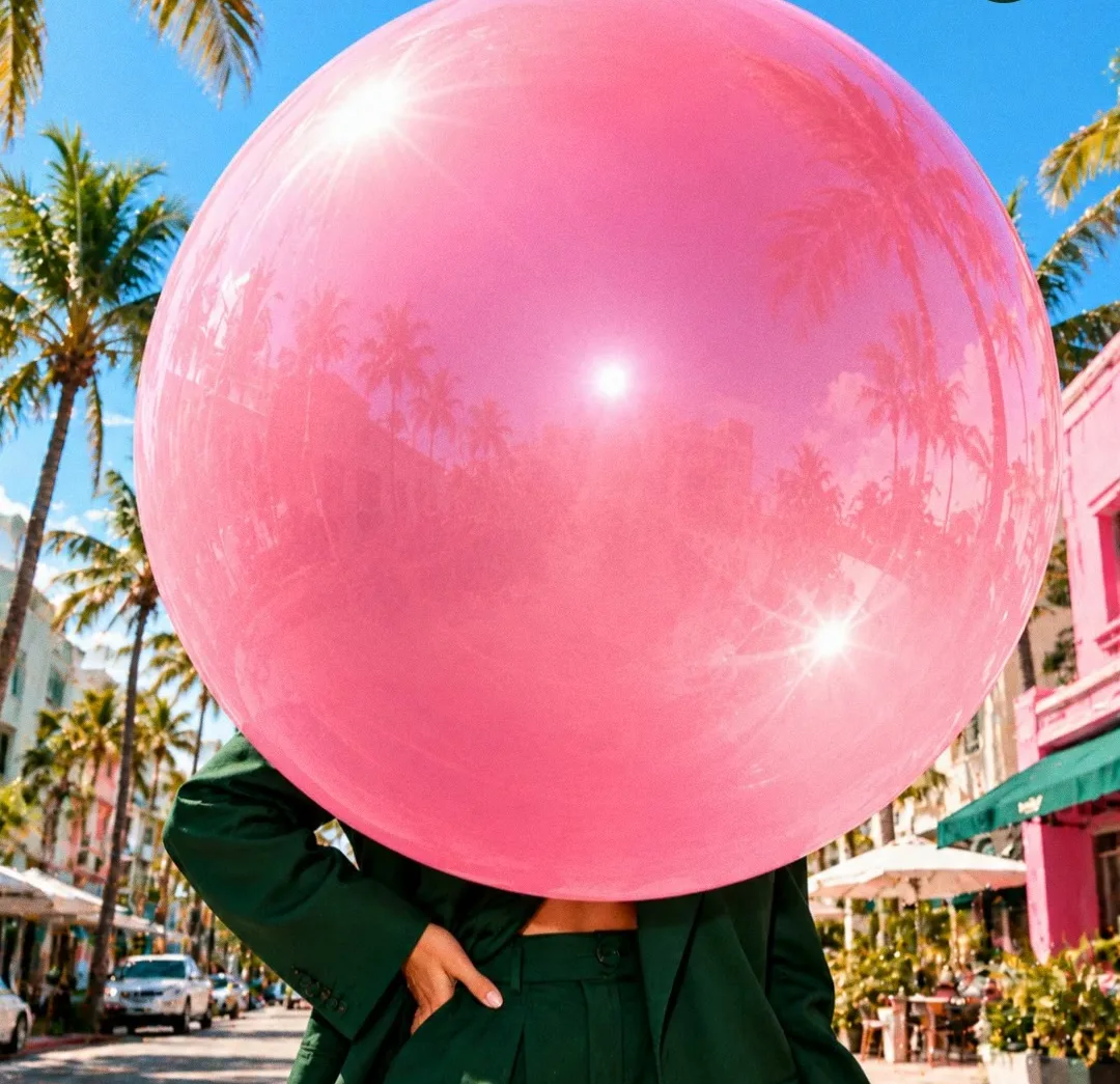 A person in a green suit whose head is hidden behind a giant pink bubblegum bubble